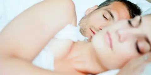 Couple peacefully sleeping in bed with white bedding