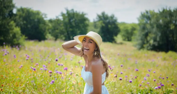A women wearing a straw hat and a white summer dress in a field laughing