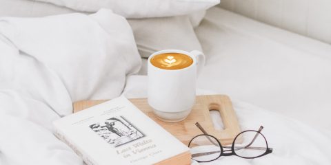 White linen bedding with a book. reading glasses and coffee cup on the bed