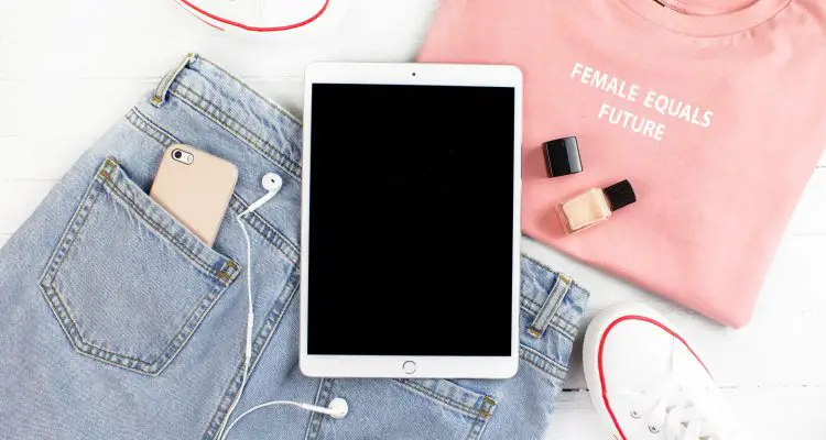 Ipad on top of a pair of denim jeans, pink t-shirt and a pair of converses next to it