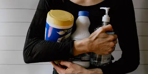 Women with a black top sitting on the floor, legs crossed holding cleaning products in her hands