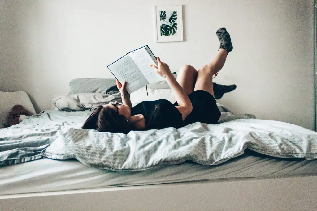 Student lying in bed reading a book 