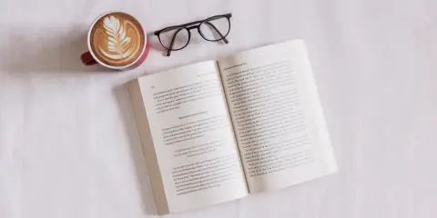 a pair of glasses, book and a cup of coffee on a bed