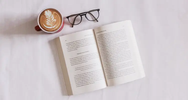 a pair of glasses, book and a cup of coffee on a bed