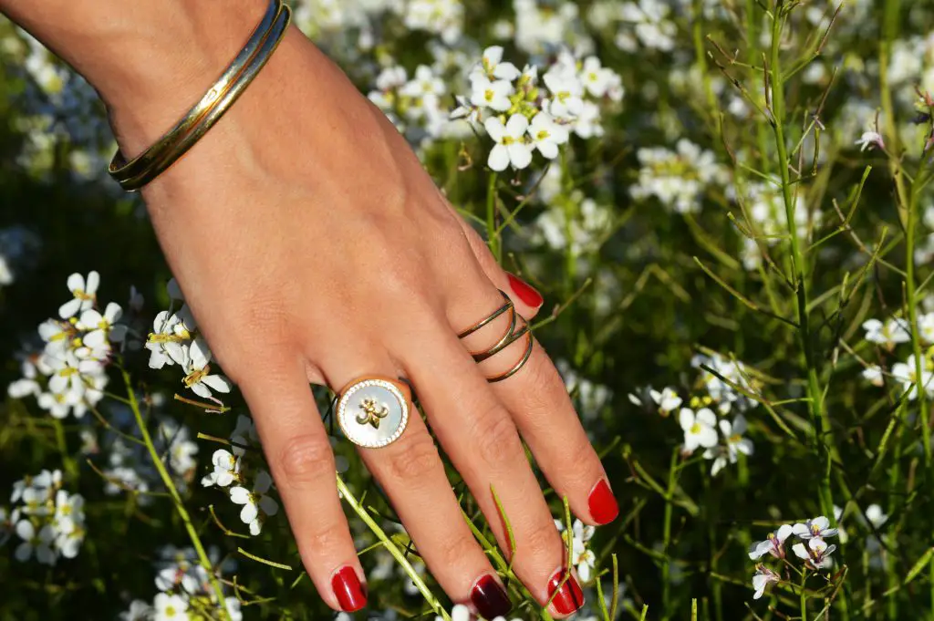 Womans hands stroking a plant with red nail polish on her fingers and rings