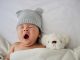 Baby sleeping with its teddy bear with a wool hat on