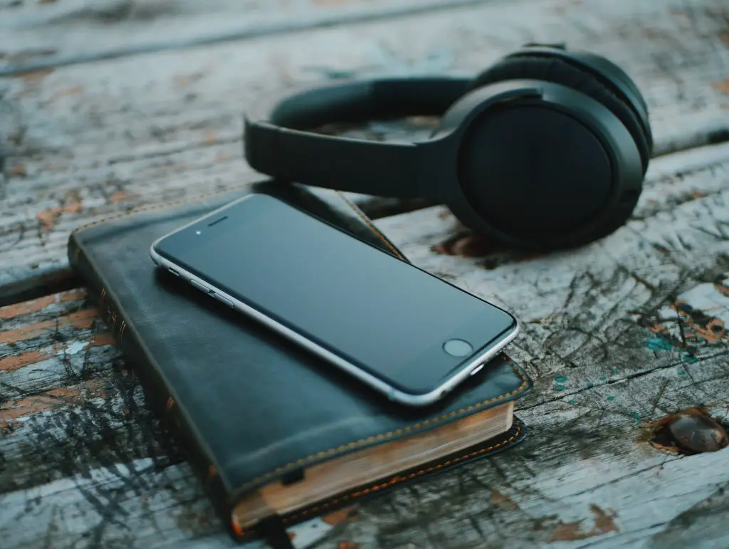 iphone, black diary and headphones on a dark wooden table
