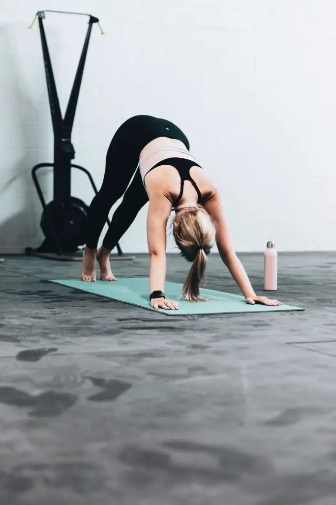 woman wearing black gym outfit doing yoga on a yoga mat with water bottle next to her 