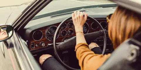 woman driving a car wearing yellow sweater and black ripped jeans